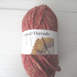 Puede incluir: Ovillo de lana acrílica Loops & Threads Charisma en tonos rojos, rosas y beige. La lana está envuelta con una etiqueta blanca que muestra el nombre de la marca y una muestra de un artículo de ganchillo.