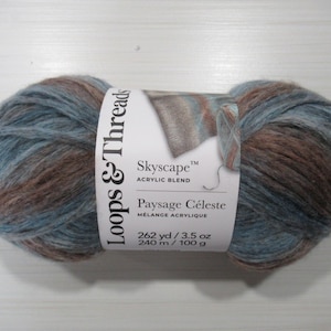 May include: A ball of Loops & Threads Skyscape acrylic blend yarn in blue and brown hues. The label reads "Paysage Céleste" and indicates 240 m / 100 g. The yarn is a mix of colours, suitable for knitting or crochet projects.