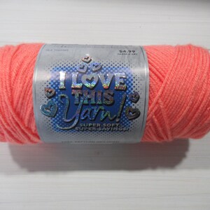 May include: A skein of bright coral-colored yarn wrapped in a paper label. The label features the text I LOVE THIS YARN! in holographic lettering, along with the phrases SUPER SOFT and SUPER SAVINGS, surrounded by small heart-shaped icons.