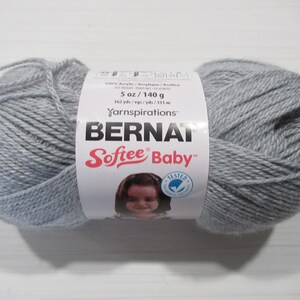 May include: A skein of Bernat Softee Baby yarn in a light gray color. The label indicates the yarn is 5 oz / 140 g. The label also features the brand name, yarn type, and a baby's face.