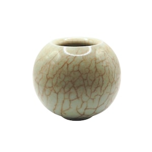 May include: A small, round, ceramic vase with a light green glaze and a network of brown crackle lines. The vase has a circular opening at the top and a smooth, glossy finish. The overall shape is spherical.