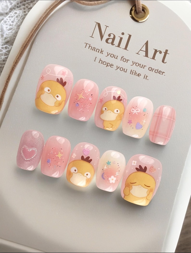 May include: A set of ten press-on nails featuring a light pink base with yellow cartoon duck characters, glitter, stars, hearts, and plaid patterns. The display card reads Nail Art, Thank you for your order. I hope you like it.