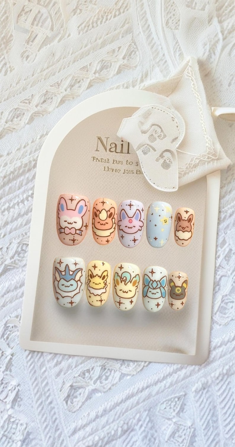 May include: A set of ten press-on nails featuring pastel-colored backgrounds and hand-painted illustrations of various cartoon creatures. Each nail is decorated with small star accents and distinct character faces, arranged on a display card.