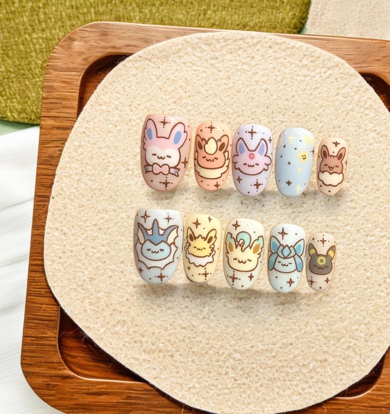May include: A set of ten press-on nails featuring pastel-colored backgrounds and various cartoon character illustrations. Each nail is decorated with small star motifs and brown outlines. The designs include diverse creatures with pointed ears and expressive faces.