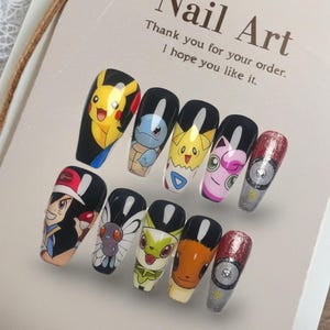 Könnte beinhalten: Ein Satz von zehn langen, Sarg-förmigen Kunstnägeln, die jeweils mit einem anderen bunten Cartoon-Charakter-Design verziert sind. Die Nägel zeigen Charaktere wie Pikachu und Ash aus der Pokemon-Serie. Der Hintergrund enthält ein Etikett mit den Worten "Nail Art".