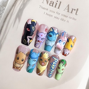Peut inclure: Ensemble de dix faux ongles longs et ovales avec une base rose. Chaque ongle est décoré d'un personnage Pokémon différent, dont Eevee, Vaporeon, Jolteon, Flareon, Espeon, Umbreon et quelques autres. Les ongles sont disposés en demi-cercle sur une surface blanche avec le texte "Nail Art" et "Merci pour votre commande. J'espère qu'il vous plaira." imprimé dessus.