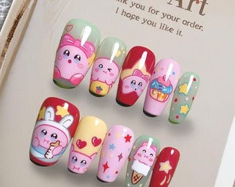 May include: A set of ten artificial nails with cartoon designs. The nails feature a variety of colors, including pink, red, yellow, and green, with images of bunnies, cupcakes, and ice cream cones. The text "Nail Art" is visible.