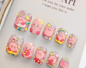 May include: Set of ten press-on nails with cartoon character designs. The nails feature a pink character with stars, rainbows, and glitter accents. The text "Nail Art" is visible on the background.