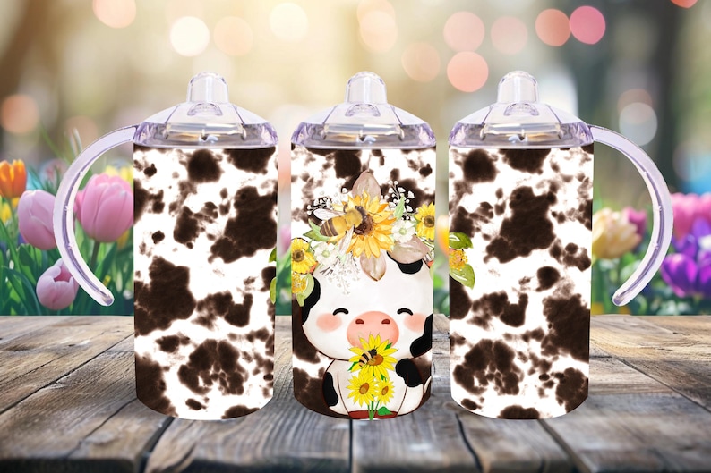 May include: Three stainless steel tumblers with a cow print design and a cute cartoon cow with a sunflower crown. The tumblers have clear lids and handles.