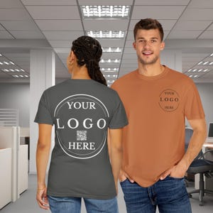 May include: Two people wearing t-shirts with the text "YOUR LOGO HERE" printed on them. One shirt is dark grey and the other is orange. The grey shirt has a QR code printed inside the circle.
