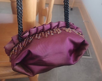 Hand made purple satin purse lined in gold satin with beaded fringe and black twisted cord handles. Zipper closure.