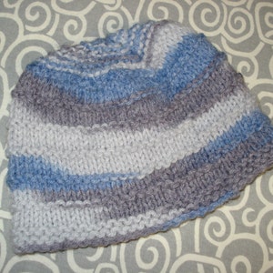 May include: A striped knitted hat in shades of gray and blue. The hat is made with a soft, textured yarn and has a simple, classic design.