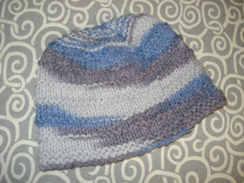 May include: A striped knitted hat in shades of gray and blue. The hat is made with a soft, textured yarn and has a simple, classic design.