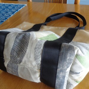 May include: A beige and gray tote bag with black straps. The bag has a patchwork design with different patterns and colors. The bag is made of a soft, fabric material.