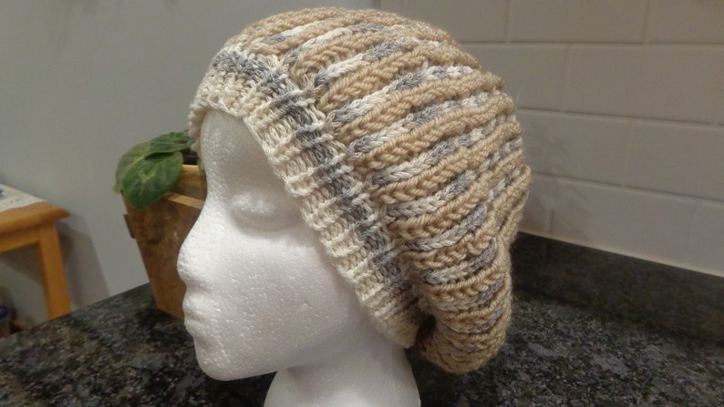 May include: A beige and gray knitted slouchy beanie hat with a ribbed texture.