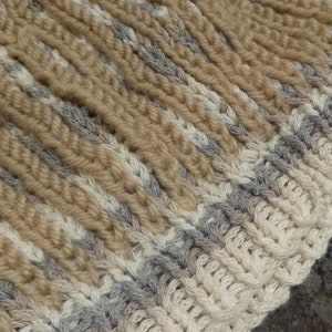 May include: A close-up of a knitted hat with a beige, white, and gray striped pattern.
