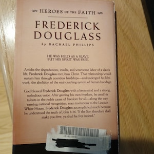 May include: A book titled "Frederick Douglass" by Rachael Phillips, part of the "Heroes of the Faith" series. The cover is a light tan color with black text. The book's description includes the quote, "He was held as a slave, but his spirit was free."