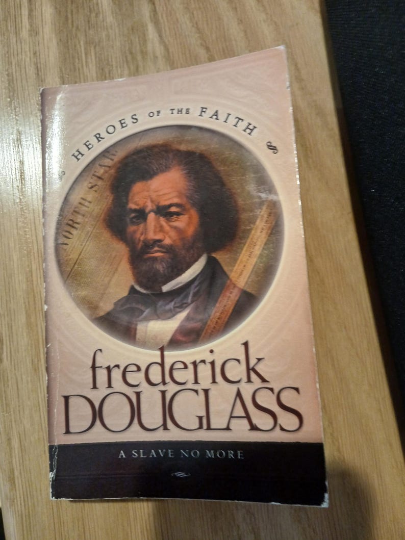 May include: A book titled "Frederick Douglass: A Slave No More" from the "Heroes of the Faith" series. The cover features a portrait of Frederick Douglass in a circular frame, with the words "North Star" around the frame.