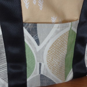 May include: A beige and green fabric tote bag with black straps. The bag has a geometric pattern with leaves and dots.