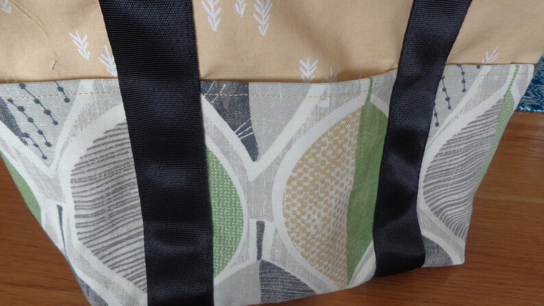 May include: A beige and green fabric tote bag with black straps. The bag has a geometric pattern with leaves and dots.