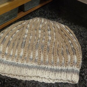 May include: A knitted hat with a beige and white striped pattern and a gray band around the bottom.