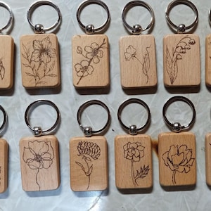 May include: Twelve wooden keychains with silver key rings. Each keychain features a different floral design, including a lily, a poppy, a daisy, and a rose.