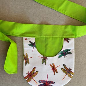 May include: A white fabric fanny pack with a lime green strap and interior. The pack is decorated with colorful dragonfly illustrations. The text "Achou achou.etsy.com" is printed on the pack.