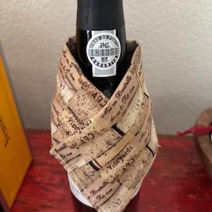 May include: A bottle of red wine with a black cap and a label that reads "VINHO DO PORTO". The bottle is wrapped with a fabric wine cozy printed with the words "Vineyards" and "Mis en Bouteille".