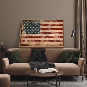 May include: A framed artwork depicting the American flag with a distressed, vintage aesthetic. The flag features red and white stripes and a blue field with white stars. The artwork is displayed above a brown sofa with green pillows.