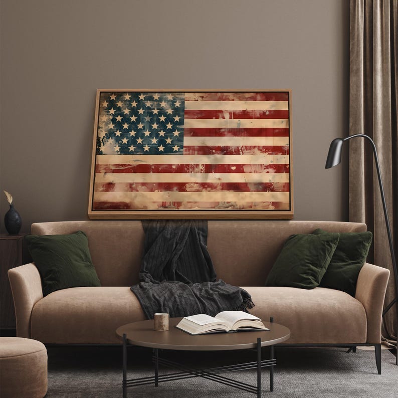 May include: A framed artwork depicting the American flag with a distressed, vintage aesthetic. The flag features red and white stripes and a blue field with white stars. The artwork is displayed above a brown sofa with green pillows.