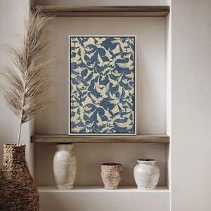 May include: A framed print with a blue and white pattern of birds flying in a flock. The print is displayed on a shelf with two white ceramic vases and a brown ceramic vase.