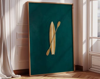 Op de afbeelding: Een ingelijste kunstdruk met een surfboard en peddel op een teal achtergrond. Het surfboard is lichtbruin met verticale strepen, en de peddel staat schuin. De lijst is goudkleurig, in een kamer met een raam.