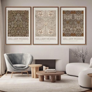 Puede incluir: Tres impresiones enmarcadas de patrones florales de William Morris en marr&oacute;n, beige y blanco. Las impresiones est&aacute;n colgadas en una pared con una chimenea blanca y un sill&oacute;n gris en primer plano.