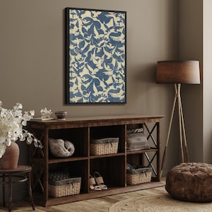 May include: A framed print of a blue and white abstract pattern featuring a repeating design of birds. The print is hanging on a wall above a wooden shelf with decorative items.