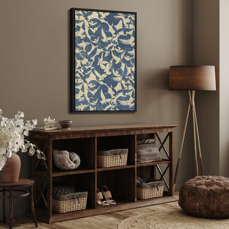 May include: A framed print of a blue and white abstract pattern featuring a repeating design of birds. The print is hanging on a wall above a wooden shelf with decorative items.