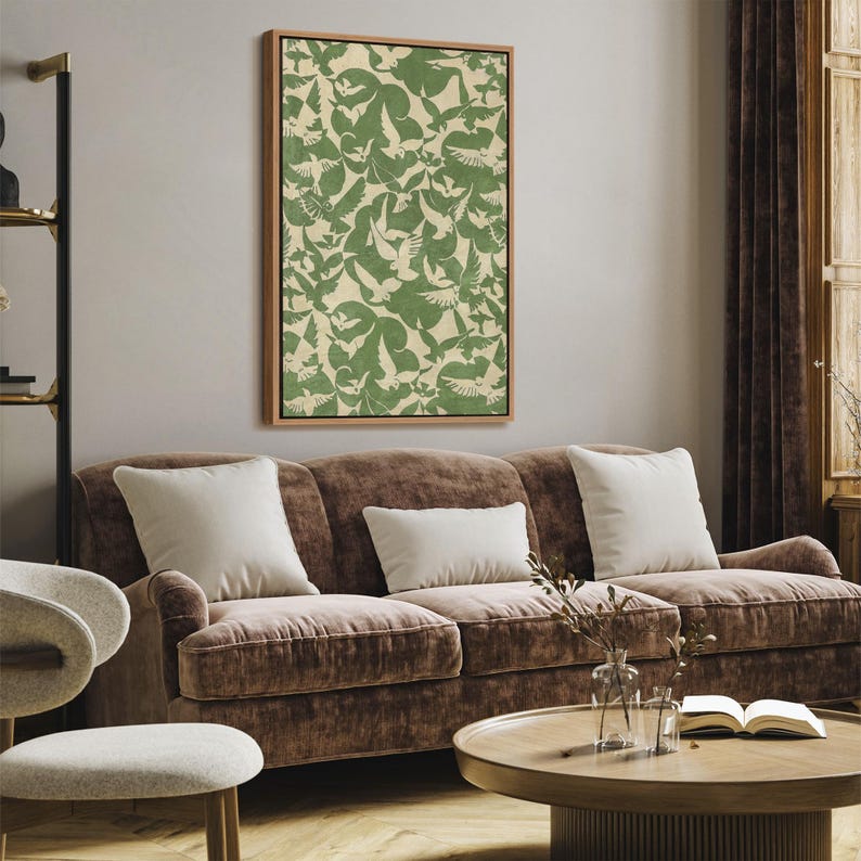 Puede incluir: Una obra de arte enmarcada con un patr&oacute;n repetido de p&aacute;jaros verdes sobre un fondo crema. La obra de arte cuelga sobre un sof&aacute; de terciopelo marr&oacute;n con cojines blancos. La habitaci&oacute;n tiene una paleta de colores neutros, con una mesa de centro de madera.
