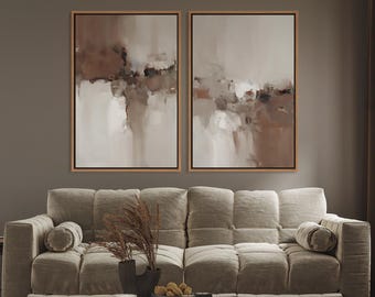 May include: Two framed abstract paintings with neutral tones of brown, beige, and white hang above a beige sofa. The paintings have a landscape-like composition. The sofa has a tufted design and is paired with a black marble coffee table.