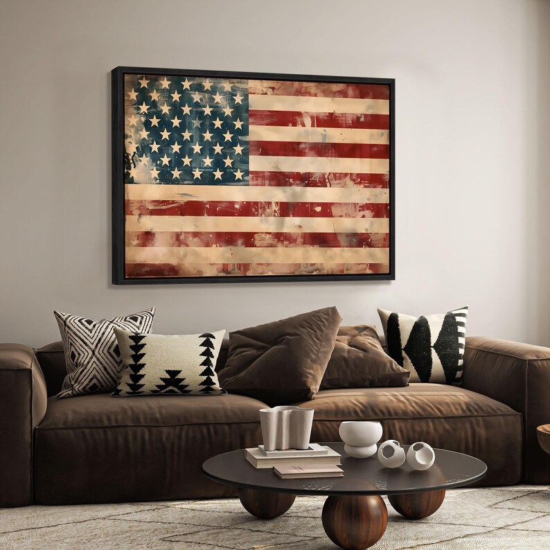 May include: Framed American flag art with a distressed, vintage look. The flag features red and white stripes and a blue field with white stars. The artwork is displayed above a brown sofa with decorative pillows.