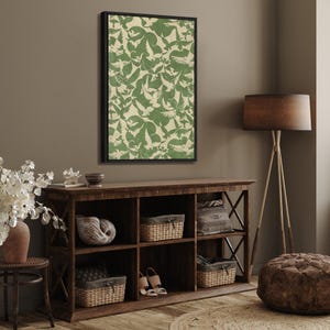 Puede incluir: Una obra de arte enmarcada con un patr&oacute;n repetido de p&aacute;jaros verdes sobre un fondo crema. La obra de arte cuelga sobre una consola de madera con cestas tejidas y objetos decorativos. Una l&aacute;mpara de pie con una pantalla marr&oacute;n est&aacute; cerca.