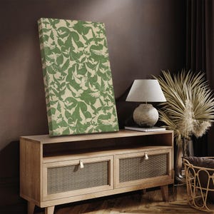 Puede incluir: Un lienzo rectangular con un patr&oacute;n repetido de p&aacute;jaros verdes sobre un fondo beige. La obra de arte se exhibe sobre un mueble de madera clara, junto con una l&aacute;mpara y elementos decorativos, creando un ambiente c&aacute;lido y acogedor.