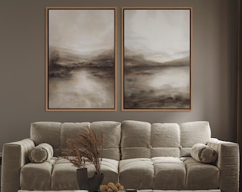 May include: Two framed landscape paintings with neutral tones hang above a beige sofa. The artwork features abstract depictions of a river and a lake, with a muted color palette of browns and creams. The sofa has a tufted design.