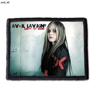 Könnte beinhalten: Ein schwarz-weißes Patch mit einem Foto von Avril Lavigne. Der Text "Avril Lavigne" und "Under My Skin" ist in Weiß auf dem Patch gedruckt.