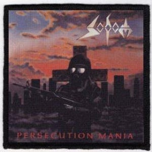 May include: A black and white patch with a dark cityscape and a figure wearing a gas mask and holding a rifle. The figure stands in front of a cross. The text "SOAD" and "PERSECUTION MANIA" are printed on the patch.