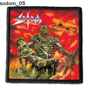 May include: A black and red embroidered patch featuring the band name "SODOM" and the text "M-16". The patch depicts a soldier carrying another soldier in a war scene with helicopters in the background.