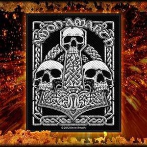 Puede incluir: Parche bordado en blanco y negro con un diseño de calavera y huesos cruzados. El parche presenta un diseño de nudo celta y el texto "Amon Amarth".