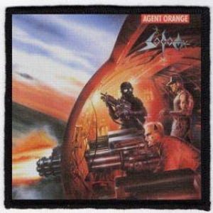 Puede incluir: Un parche en blanco y negro con el logotipo de una banda. El logotipo es una imagen estilizada de una calavera con una corona en la parte superior. El texto "AGENT ORANGE" está por encima de la calavera. El fondo es una puesta de sol roja y naranja con una nave espacial futurista en el fondo.