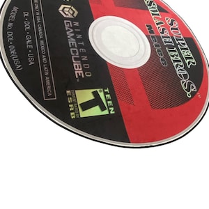 May include: A red and black GameCube disc with the text "SUPER SMASH BROS. Melee" and "NINTENDO GAMECUBE" printed on it. The disc is rated "T" for Teen by the ESRB.