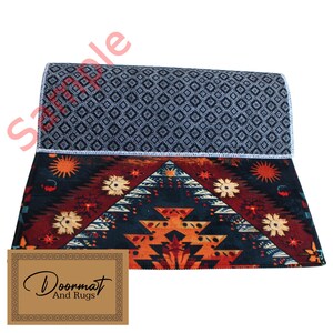 May include: A colourful doormat with a geometric pattern in shades of red, orange, yellow, blue, and white. The doormat has a black background and a white border. The text "Doormat And Rugs" is printed on a brown tag in the bottom right corner of the image.