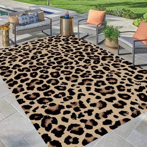 May include: A beige and black leopard print area rug with a modern design. The rug is laid out on a patio with patio furniture.