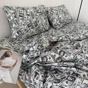 Könnte beinhalten: Bettwäsche-Set mit einem sich wiederholenden Muster aus US-Zwanzig-Dollar-Scheinen in Grün, Schwarz und Weiß. Das Set enthält einen Bettbezug und zwei Kissenbezüge. Die Bettwäsche ist aus einem weichen Stoff, möglicherweise Baumwolle.